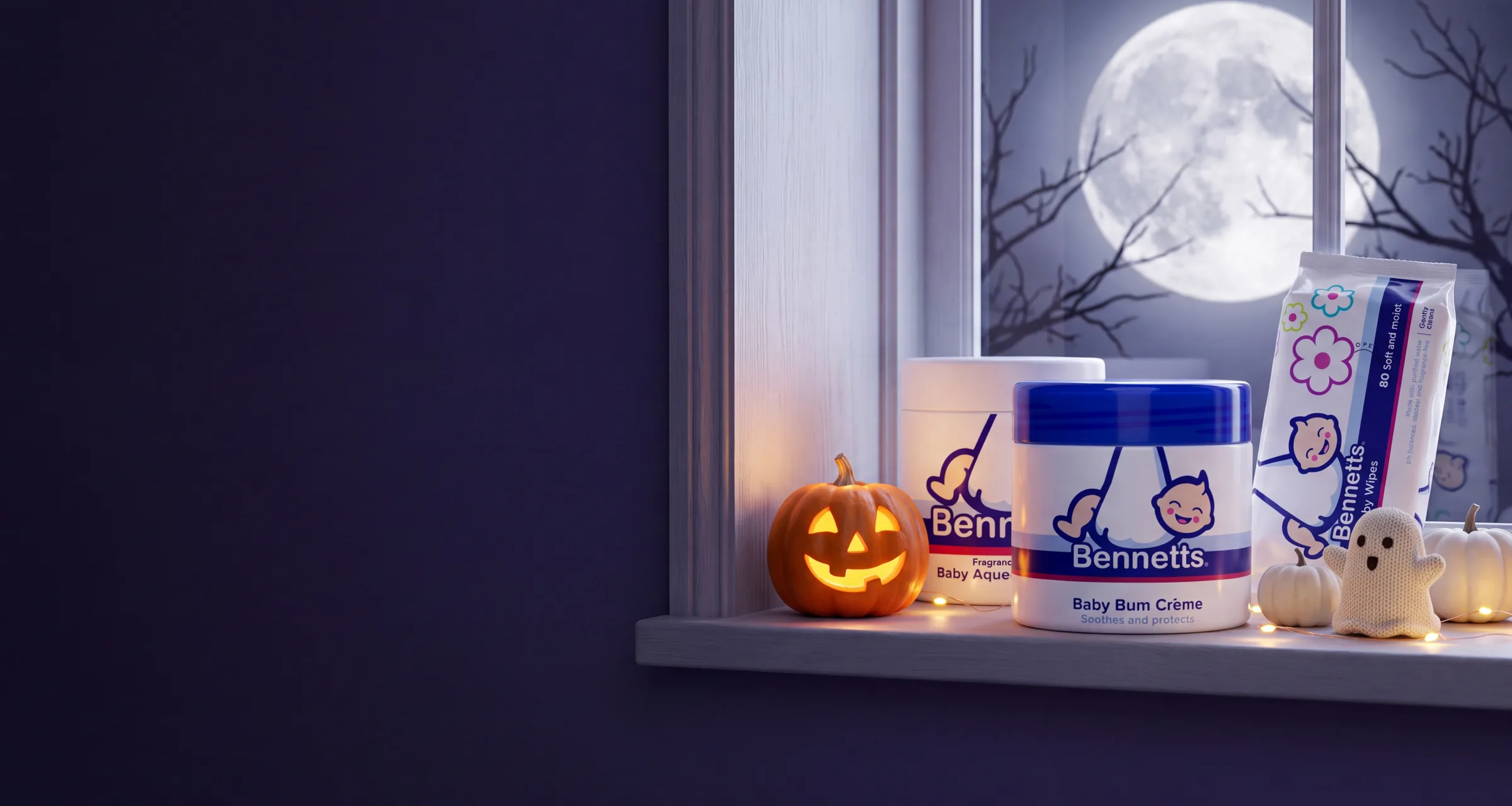 Bennetts Baby Bum Crème, Baby Aqueous Cream and Baby Wipes on a nursery windowsill under a full moon, with a glowing jack-o’-lantern, little pumpkins and a knitted ghost
